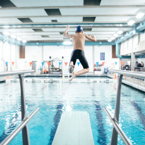 A twelve year old boy enjoys time at the swimming pool jumping off of a diving board into the water. Healthy active lifestyle that is fun as well.
